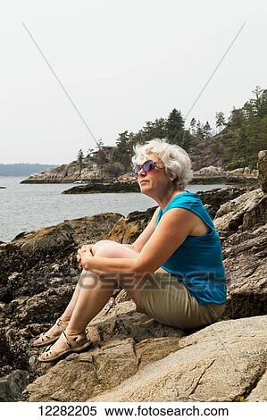 Woman sitting on rocks at the water's edge looking out over the coast; Bowen Island, British Columbia, Canada View Large Photo Image Stock Photography - Woman sitting on rocks at the water's edge looking out over the coast; Bowen Island, British Columbia, Canada. Fotosearch