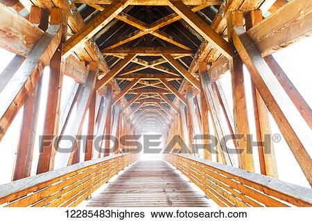 Stock Photograph - Wooden bridge with sunlight glowing at the end; Golden, British Columbia, Canada. Fotosearch