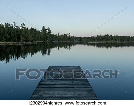 Stock Photograph - Wooden dock leading out to a tranquil lake at sunrise; Whiteshell, Manitoba, Canada. Fotosearch
