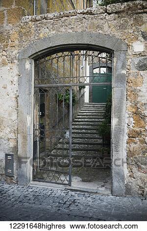 Stock Photograph - Worn and weathered old stone walls with an open gate leading to steps and a green door; Orvieto, Umbria, Italy. Fotosearch