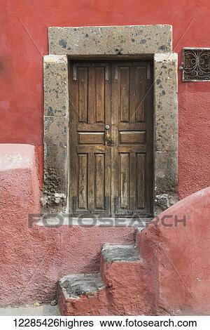 Stock Photograph - Worn wooden doors on a red painted building; San Miguel de Allende, Guanajuato, Mexico. Fotosearch