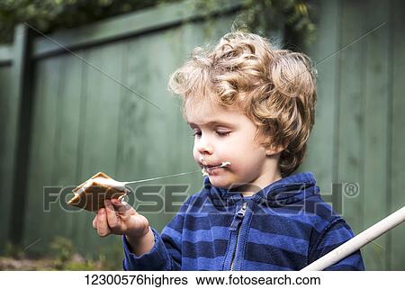 Stock Photograph - Young boy eating a s'more outdoors and getting sticky; St. Albert, Alberta, Canada. Fotosearch