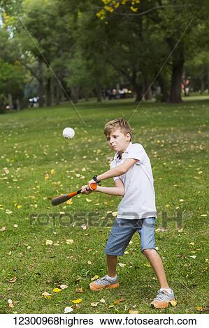 Stock Photograph - Young boy hitting a baseball in a park; Edmonton, Alberta, Canada. Fotosearch