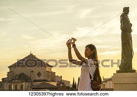 Stock Photograph - Young Chinese woman taking a picture with her phone; Cuenca, Castile-La Mancha, Spain. Fotosearch