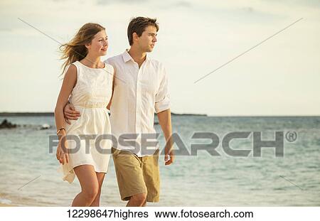 Young couple in love, Attractive man and woman enjoying romantic evening walk on the beach, Watching the sunset View Large Photo Image Stock Photograph - Young couple in love, Attractive man and woman enjoying romantic evening walk on the beach, Watching the sunset. Fotosearch