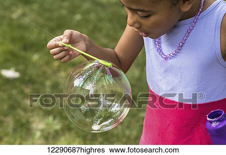 Stock Photograph - Young girl blowing a large bubble through a bubble wand; Edmonton, Alberta, Canada. Fotosearch