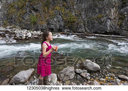 Stock Photograph - Young girl blowing bubbles along the Little Susitna river near Hatcher Pass, Southcentral Alaska, autumn. Fotosearch