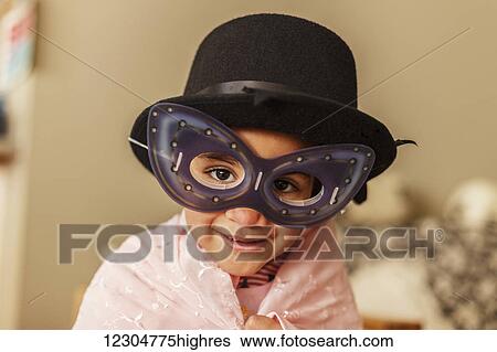 Stock Photograph - Young girl playing dress up wearing a mask and hat; Edmonton, Alberta, Canada. Fotosearch