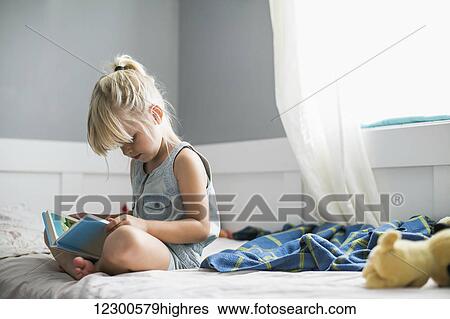 Stock Photograph - Young girl sitting on her bed reading a children's Bible; Langley, British Columbia, Canada. Fotosearch