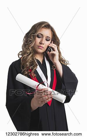 Stock Photograph - Young graduating woman holding her diploma and talking on her smart phone; Edmonton, Alberta, Canada. Fotosearch