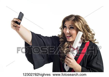 Stock Photograph - Young graduating woman taking a self-portrait with her smart phone and celebrating her graduation; Edmonton, Alberta, Canada. Fotosearch
