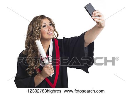 Stock Photograph - Young graduating woman taking a self-portrait with her smart phone and celebrating her graduation; Edmonton, Alberta, Canada. Fotosearch