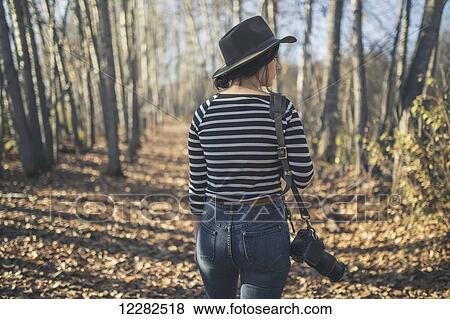 Stock Photo - Young woman wearing hat with camera and walking through the woods near Creamer's Field, Fairbanks, Interior Alaska, Autumn. Fotosearch
