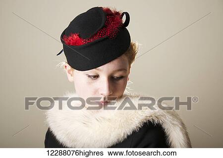 Stock Photograph - Young woman with red hair in a black hat with red feathers and white fur; Caldecott, England. Fotosearch