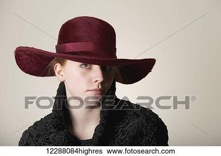 Stock Photograph - Young woman with red hair in maroon hat and black coat; Caldecott, England. Fotosearch