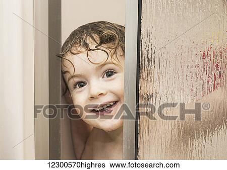 Stock Photograph - Youngster smiling and peeking out from behind a glass shower door in a bathroom; St. Albert, Alberta, Canada. Fotosearch