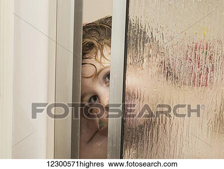 Stock Photograph - Youngster smiling and peeking out from behind a glass shower door in a bathroom; St. Albert, Alberta, Canada. Fotosearch