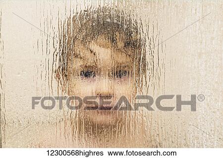 Stock Photograph - Youngster smiling and peering out through the glass on a shower door in a bathroom; St. Albert, Alberta, Canada. Fotosearch
