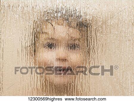 Stock Photograph - Youngster smiling and peering out through the glass on a shower door in a bathroom; St. Albert, Alberta, Canada. Fotosearch