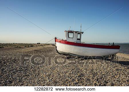Stock Image - A boat on a shingle beach; Dungeness, Kent, England. Fotosearch