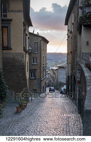 A car drives down a cobblestone street at sunrise between residential buildings; Orvieto, Umbria, Italy View Large Photo Image Stock Photograph - A car drives down a cobblestone street at sunrise between residential buildings; Orvieto, Umbria, Italy. Fotosearch