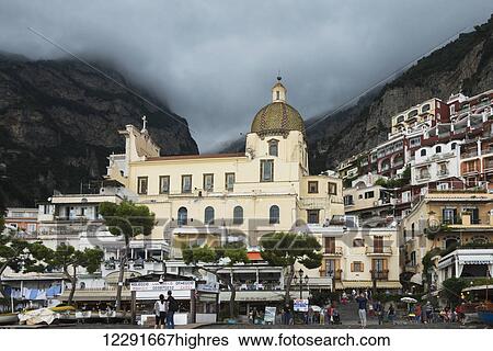 Stock Photograph - A church building and houses on a hillside with pedestrians along the Amalfi coast; Positano, Campania, Italy. Fotosearch