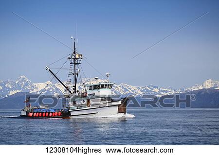 Stock Photograph - A commercial fishing boat on the waters of Main Bay, with the Chugach Mountains in the background, Prince William Sound, Whittier, Southcentral Alaska, USA. Fotosearch