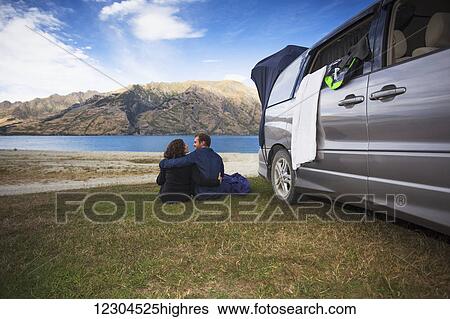 Stock Photograph - A couple sits outside their camper van at Kidds Bush campsite at Lake Hawea; Hunter Valley, Otago, New Zealand. Fotosearch