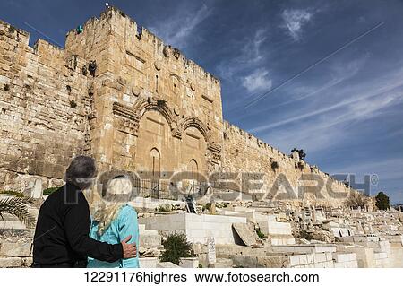 Stock Photograph - A couple stands looking at the Eastern gate of the Temple Mount, Old city Jerusalem; Jerusalem, Israel. Fotosearch