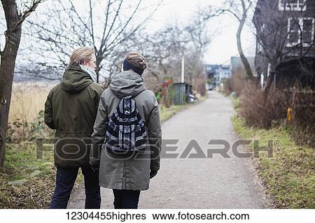 Stock Photograph - A couple walks down a path in the bohemian neighbourhood of Christianshavn, where residents consider their community to be a separate entity apart from Copenhagen; Christianshavn, Denmark. Fotosearch