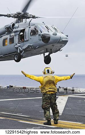 Stock Photograph - A crewman onboard the USS Peleliu (LHA-5) guides a MH-60S Knighthawk helicopter in for a landing; Hawaii, United States of America. Fotosearch