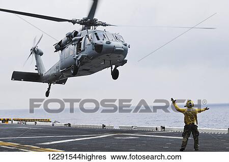 A crewman onboard the USS Peleliu (LHA-5) guides a MH-60S Knighthawk helicopter in for a landing; Hawaii, United States of America View Large Photo Image Stock Photograph - A crewman onboard the USS Peleliu (LHA-5) guides a MH-60S Knighthawk helicopter in for a landing; Hawaii, United States of America. Fotosearch