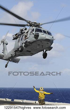 Stock Photograph - A crewman onboard the USS Peleliu (LHA-5) guides a MH-60S Knighthawk helicopter in for a landing; Hawaii, United States of America. Fotosearch
