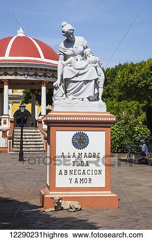 Stock Photograph - A dog sunbathes in front of a monument which says 'To all the loving and self-sacrificing mothers', dedication statue in Central Park; Granada, Nicaragua. Fotosearch