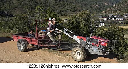 Stock Photograph - A father with his young children riding on a piece of farm equipment; Paro, Bhutan. Fotosearch