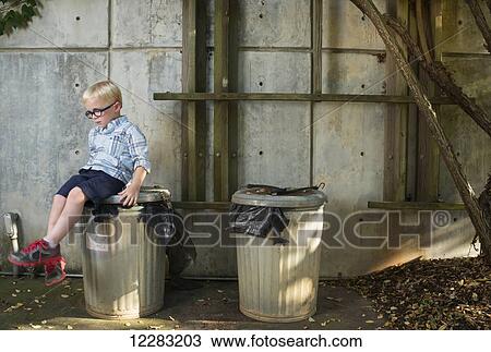 Stock Image - A five-year-old boy sits on a metal garbage can at JC Raulston Arboretum; Raleigh, North Carolina, USA. Fotosearch