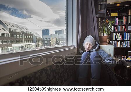 Stock Photograph - A girl sits on the floor of an apartment with a view out the window; Reykjavik, Iceland. Fotosearch