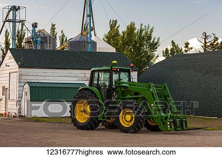 Stock Photograph - A green tractor sits on a farm outside a barn and silos; Herschel, Saskatchewan, Canada. Fotosearch