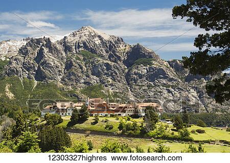 Stock Photograph - A large resort hotel on top of a green hill, with a mountain in the background; Bariloche, Argentina. Fotosearch