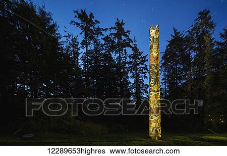 Stock Photograph - A large Totem Pole lit up at night in Sitka National Historic Park, Sitka, Southeast Alaska, USA, Summer. Fotosearch