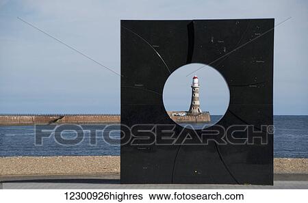 Stock Photograph - A lighthouse viewed through a round hole in a black sculpture; Sunderland, Tyne and Wear, England. Fotosearch