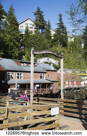 Stock Photograph - A man, 60's, and a woman, 60's walk under the Creek Street sign in downtown Ketchikan, Southeast Alaska, USA, Spring. Fotosearch
