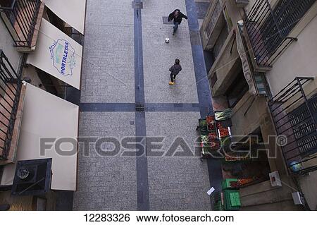 A man and child play football (soccer) in a side street in the old town, near fruit and vegetables arranged outside a grocery store; San Sebastian, Spain View Large Photo Image Stock Photograph - A man and child play football (soccer) in a side street in the old town, near fruit and vegetables arranged outside a grocery store; San Sebastian, Spain. Fotosearch