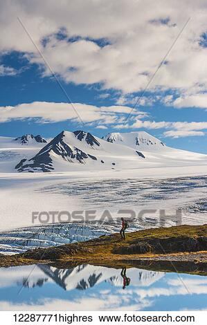 Stock Photograph - A man hiking by a lake with the Harding Icefield and the Nunatak peaks in the background, Kenai Fjords National Park, Southcentral Alaska. Fotosearch