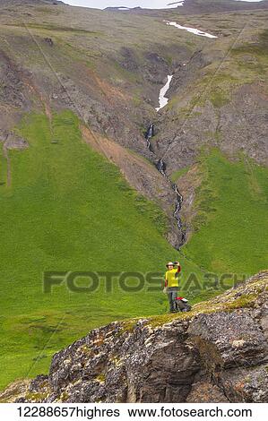 Stock Photograph - A man hiking in Hanging Valley takes a selfie with a waterfall in the background in South Fork near Eagle River, Southcentral Alaska, summer. Fotosearch