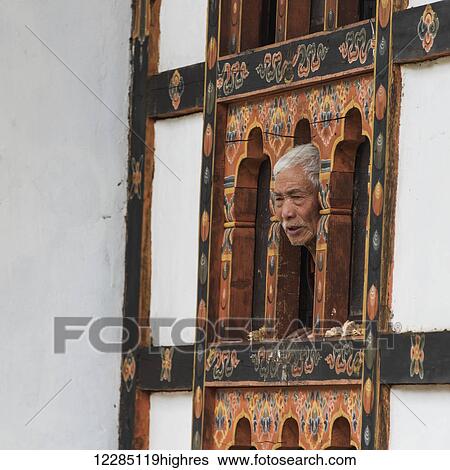 Stock Photograph - A man peers out a window from a wall with hand painted facade, Tachog Lhakhang Dzong; Paro, Bhutan. Fotosearch