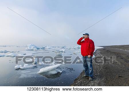 A man standing on the coast of the Arctic Ocean during a foggy sunset talks on his cell phone with sea ice floating in the background; Barrow; North Slope; Arctic Alaska; USA; Summer View Large Photo Image Stock Photograph - A man standing on the coast of the Arctic Ocean during a foggy sunset talks on his cell phone with sea ice floating in the background; Barrow; North Slope; Arctic Alaska; USA; Summer. Fotosearch