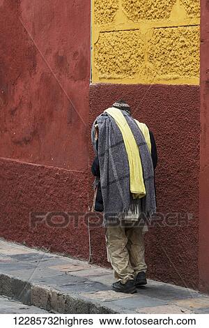 Stock Photograph - A man walks down a sidewalk beside a red and yellow painted building; San Miguel de Allende, Guanajuato, Mexico. Fotosearch