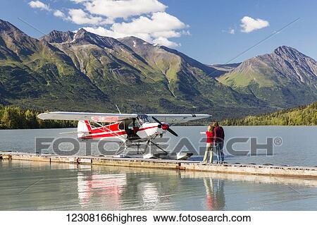 Stock Photograph - A Mother with her daughter looking at a float plane docked at the Trail Lake Float Plane Base on a clear day, the Kenai Mountains in the background, Kenai Peninsula, Southcentral Alaska, USA, Summer. Fotosearch