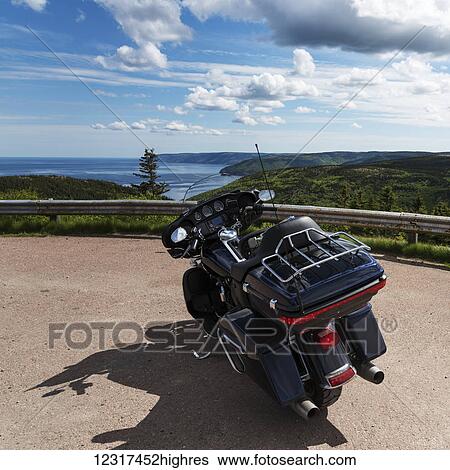 Stock Photograph - A motorcycle parked at a roadside lookout with a view of the coastline and ocean, Cape Breton Highlands National Park; Pleasant Bay, 0va Scotia, Canada. Fotosearch